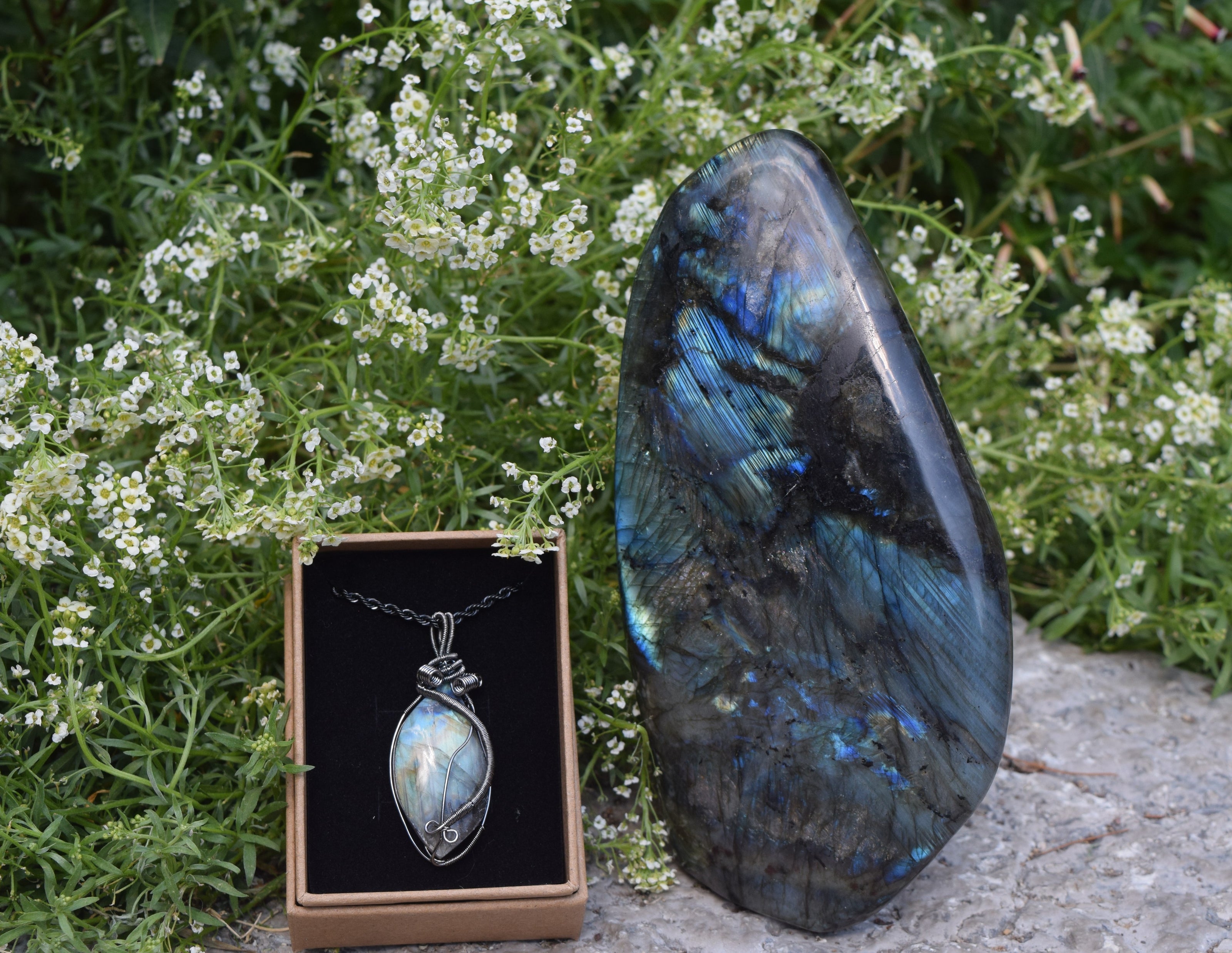 A crystal necklace displayed inside of a box, next to a crystal stone