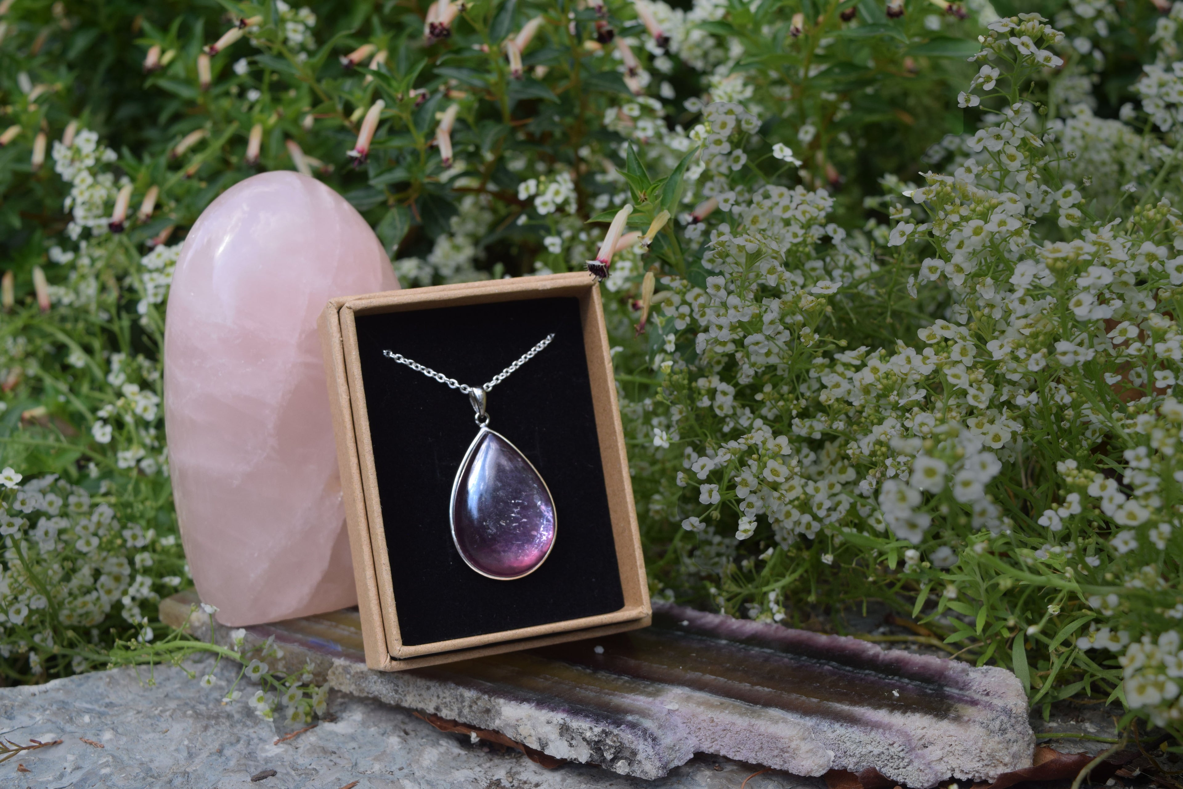 Purple iridescent crystal necklace, inside a box, leaning on a pink rose quartz  